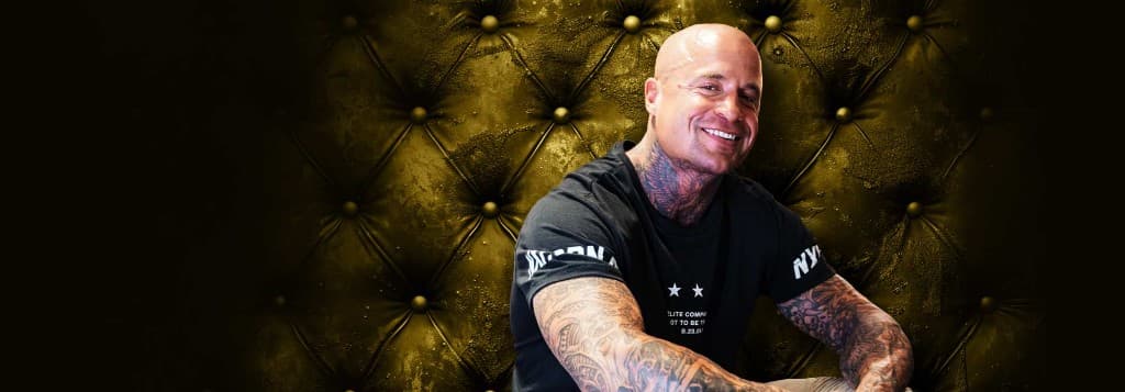 Nick Midgley smiling, tattoos visible, gold tufted backdrop with dark vignette